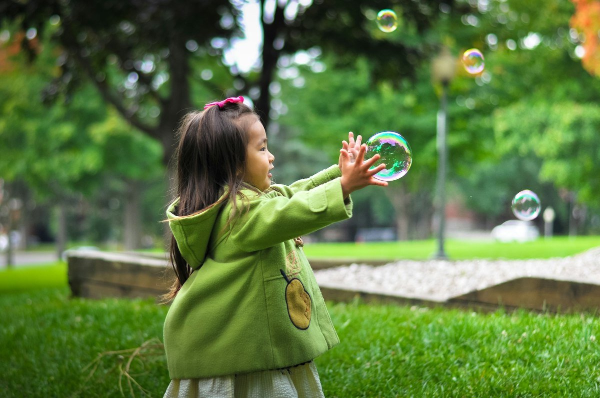 Child playing with soap bubbles in a green park
